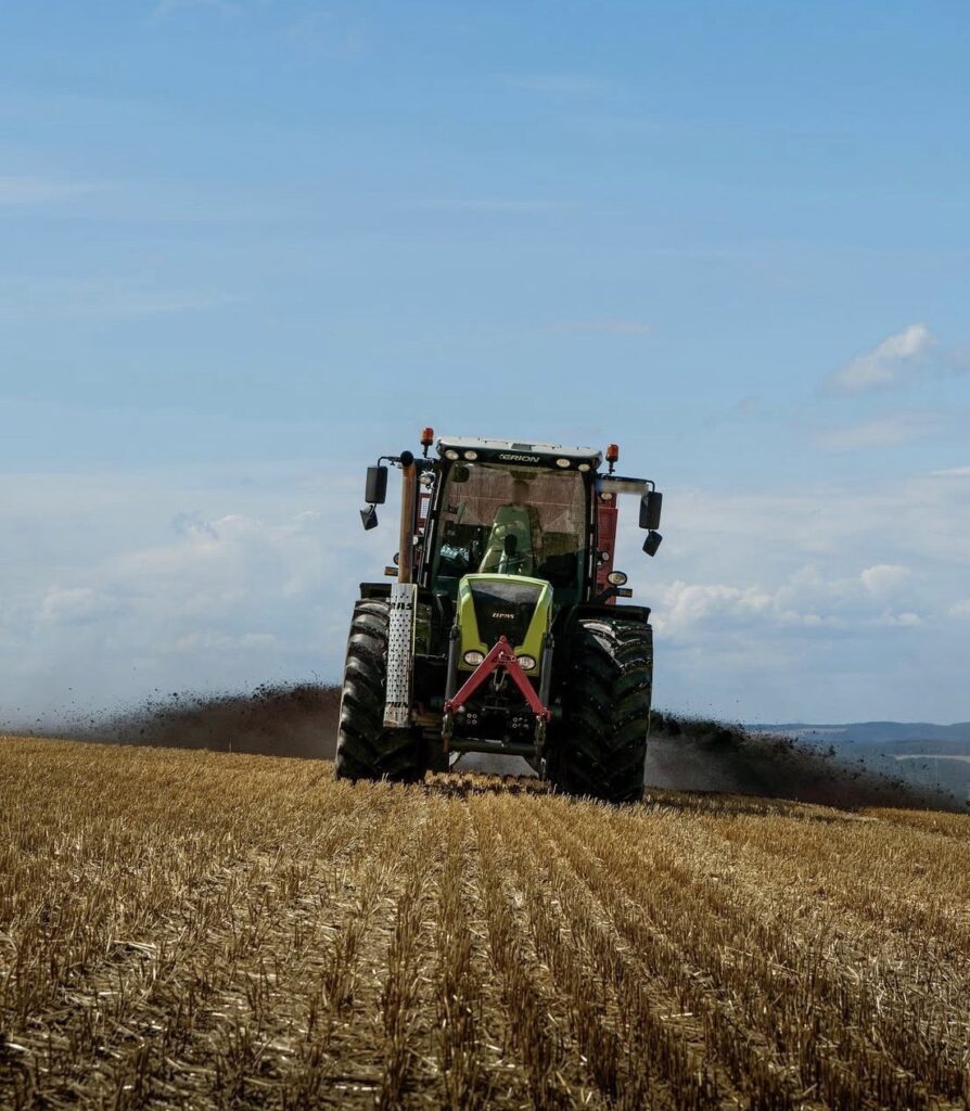 Traktor fährt über ein abgeerntetes Stoppelfeld im Erzgebirge und zieht eine dunkle Staubfahne hinter sich her